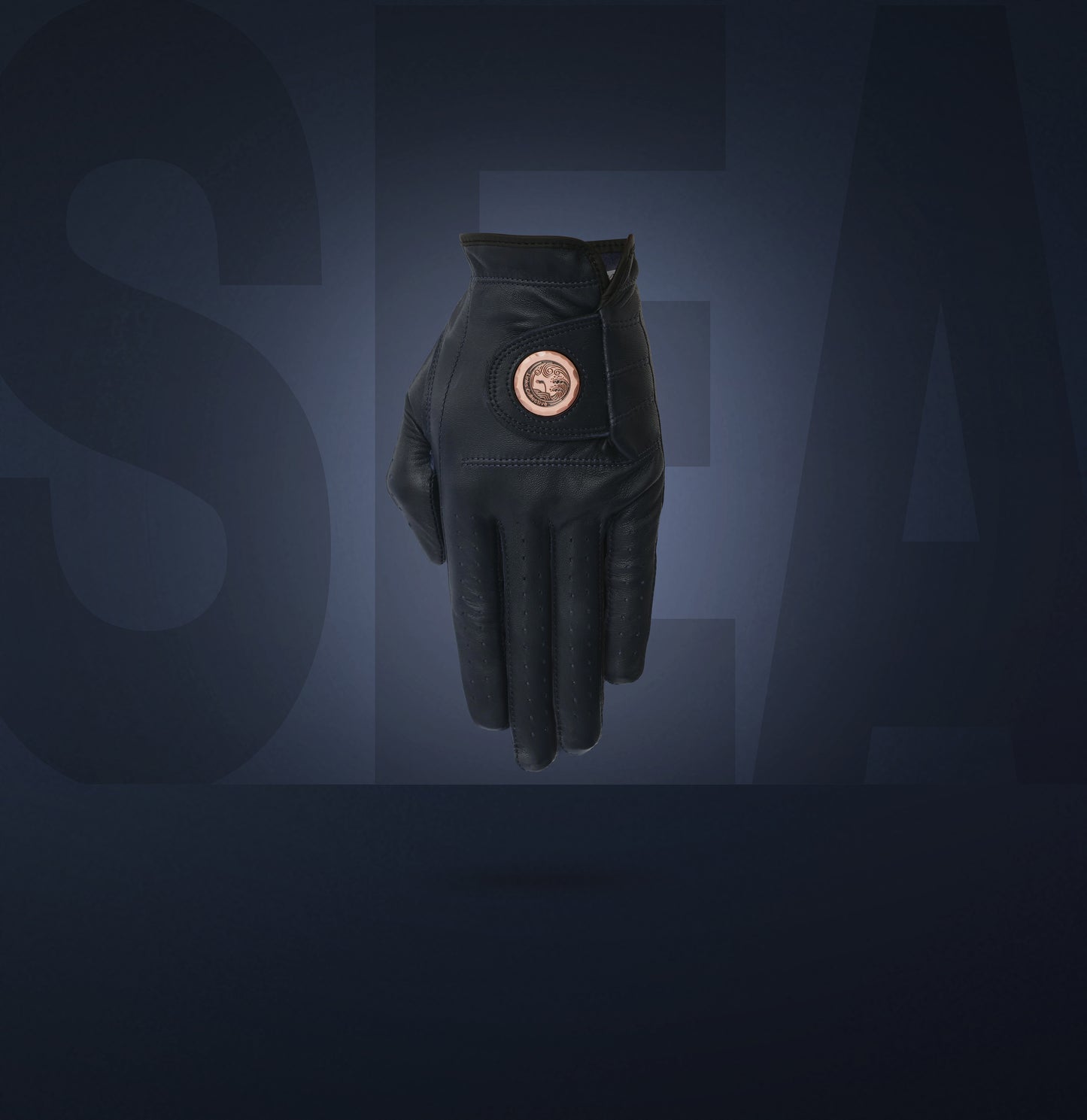 A blue cabretta leather golf glove with a forged metal ball marker attached, set against a dark background with the collection name 'SEA' visible in the background.