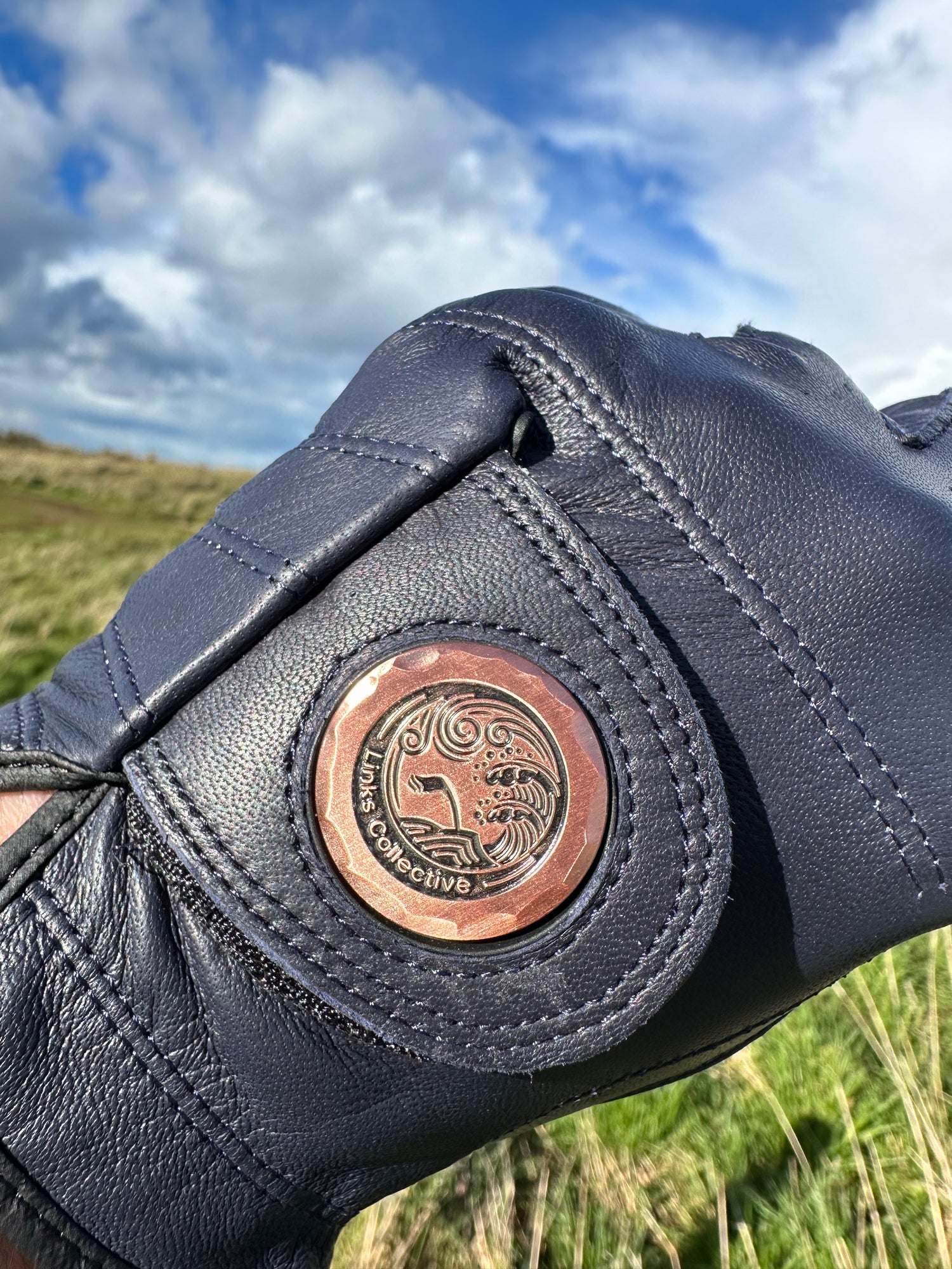 A man wearing a Links Collective blue leather golf glove while holding a golf club on a sunny green golf course.